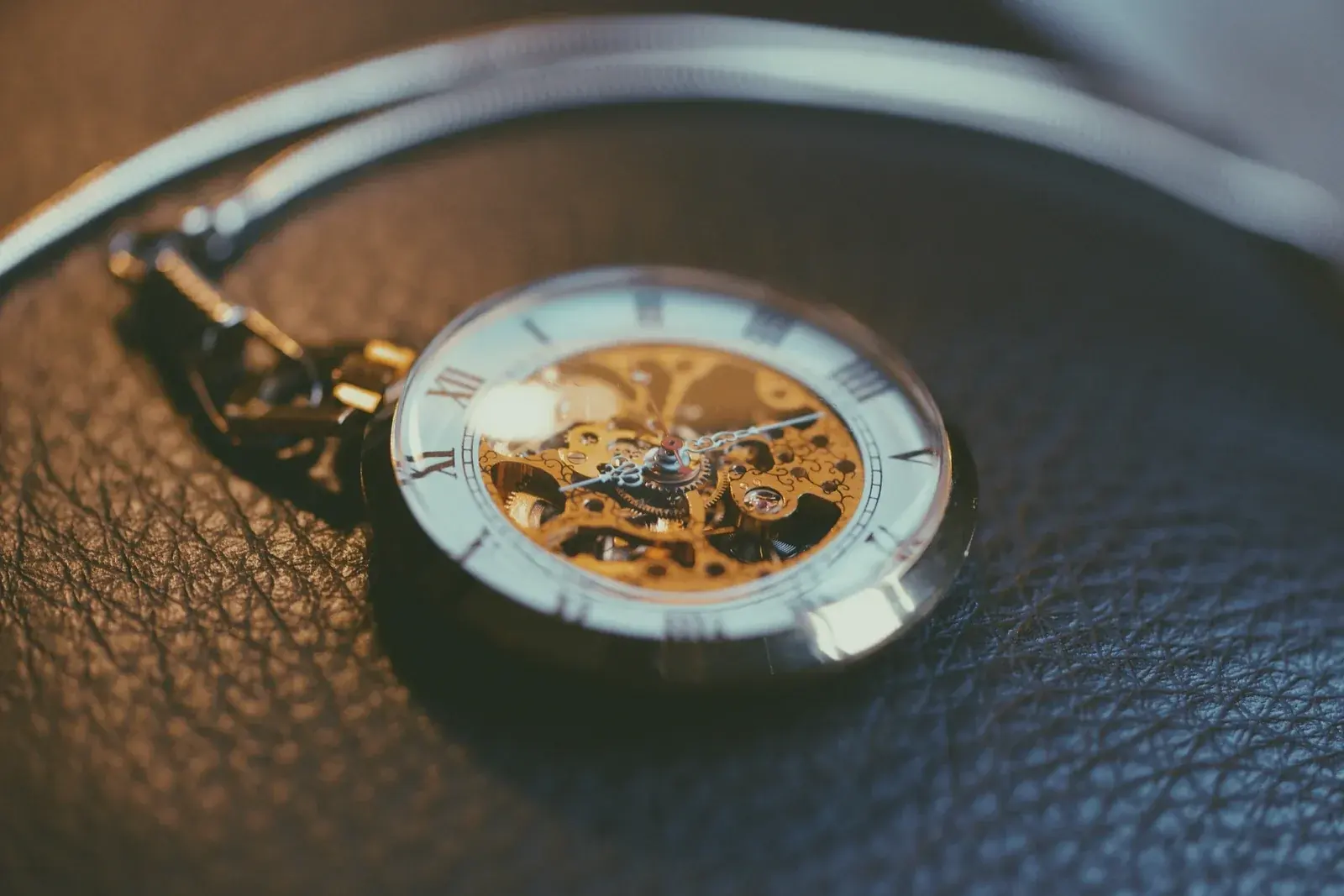 A skeleton pocket watch with Roman numerals and its chain laid on textured black leather