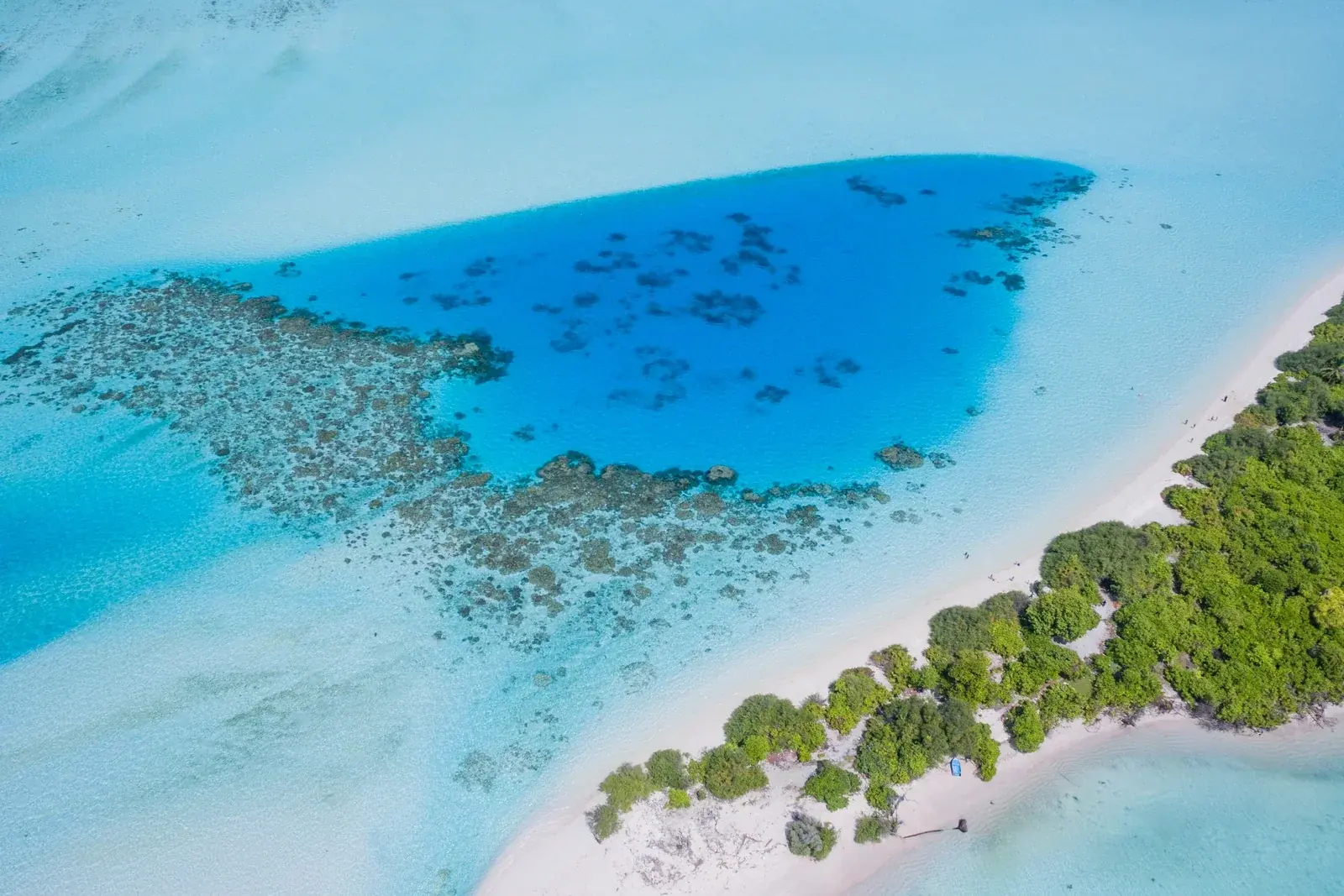 Aerial view of a Maldivian island edged with white sand beside a turquoise lagoon and coral reef