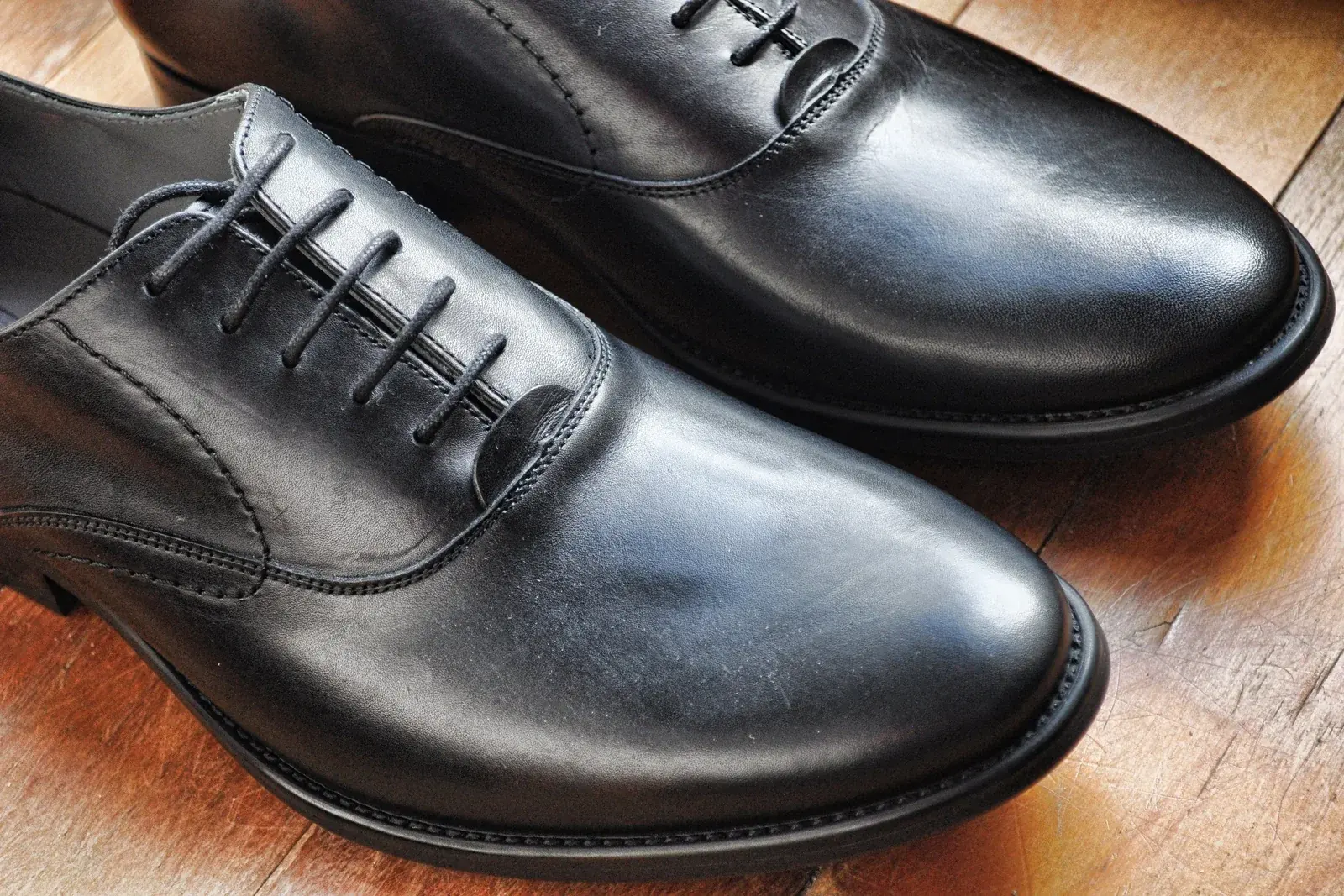 A pair of polished black leather Oxford shoes on a worn wooden floor