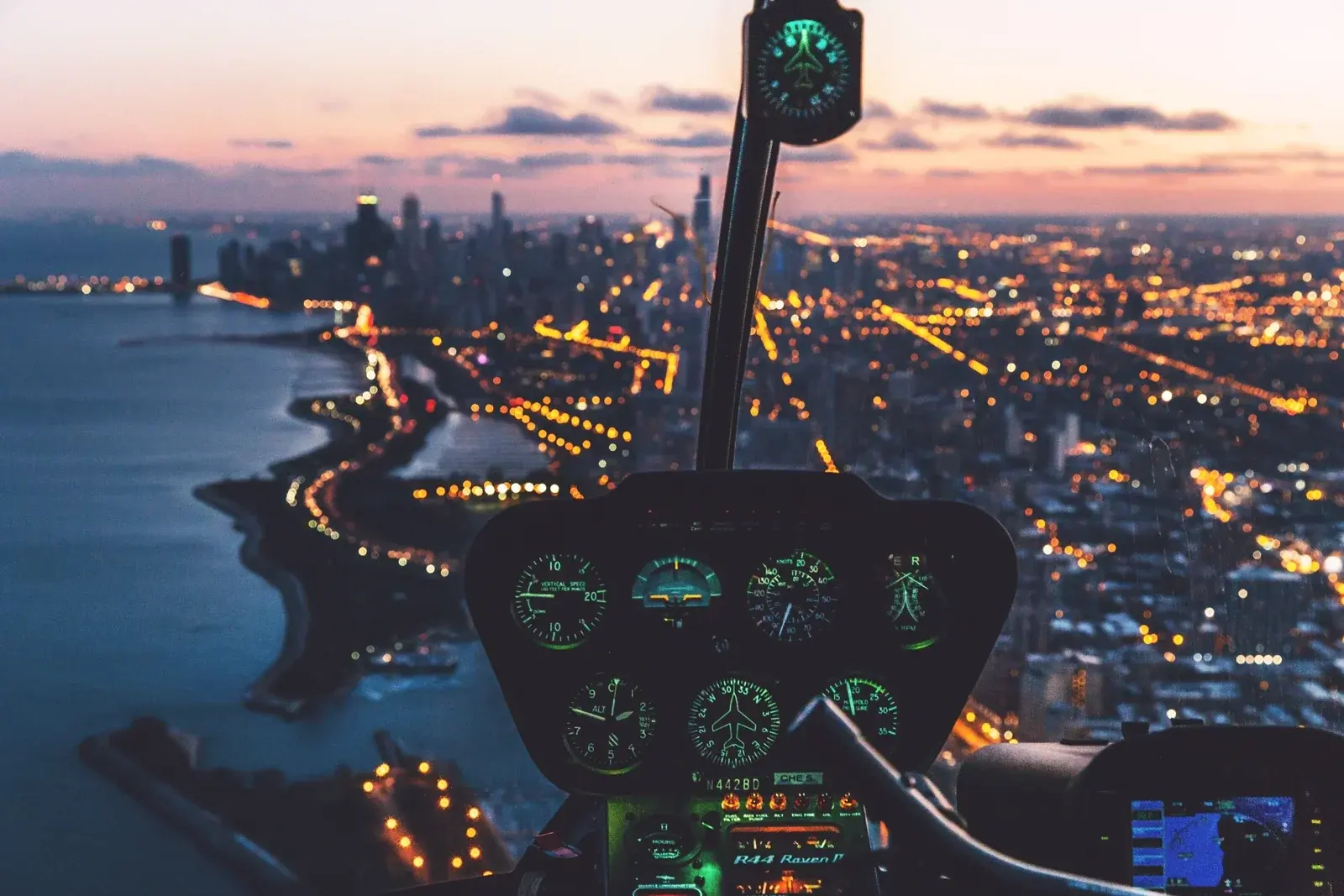 A helicopter instrument panel glowing green over a lakeside city skyline at dusk