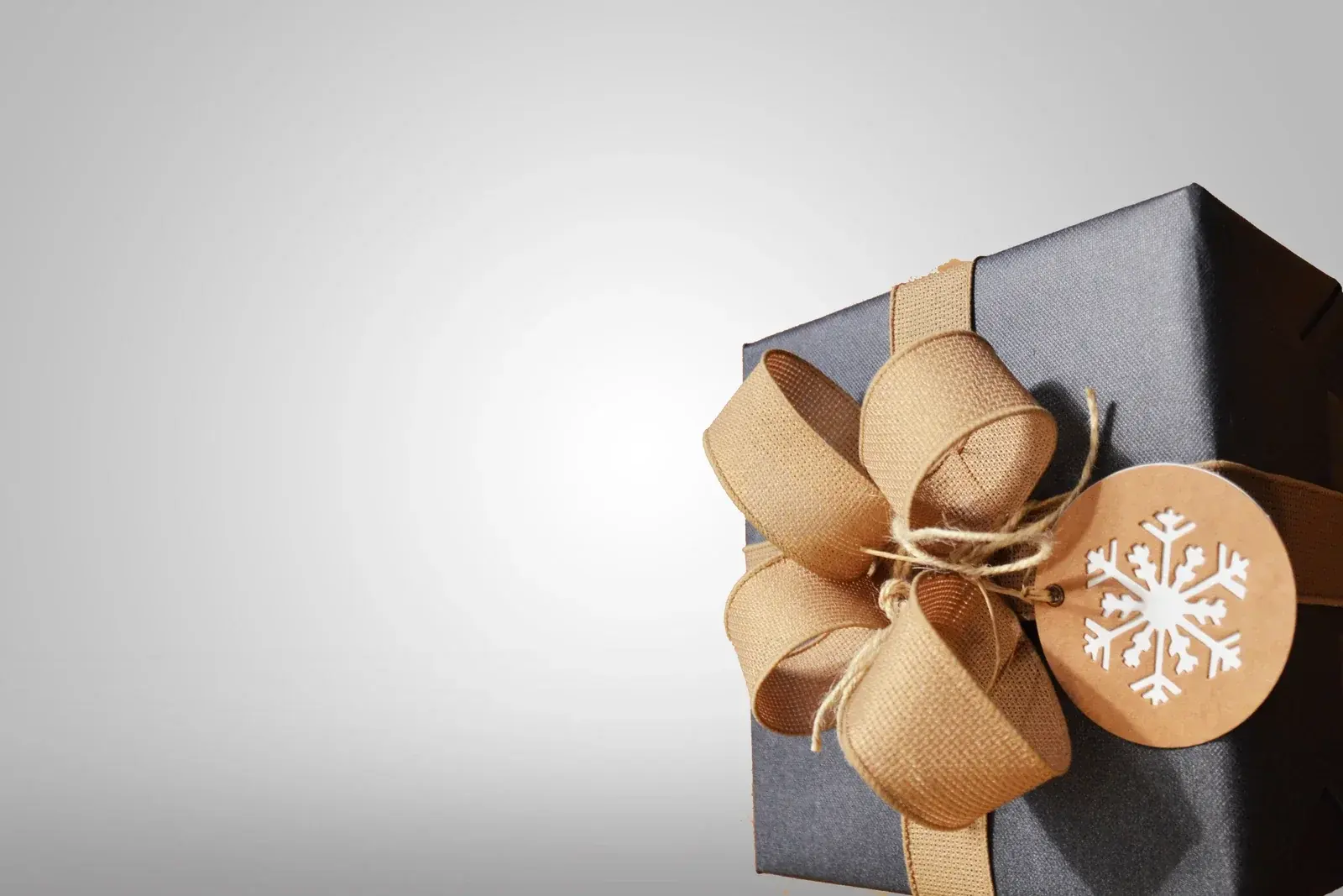 A charcoal gift box tied with a wide burlap bow and a kraft tag printed with a white snowflake