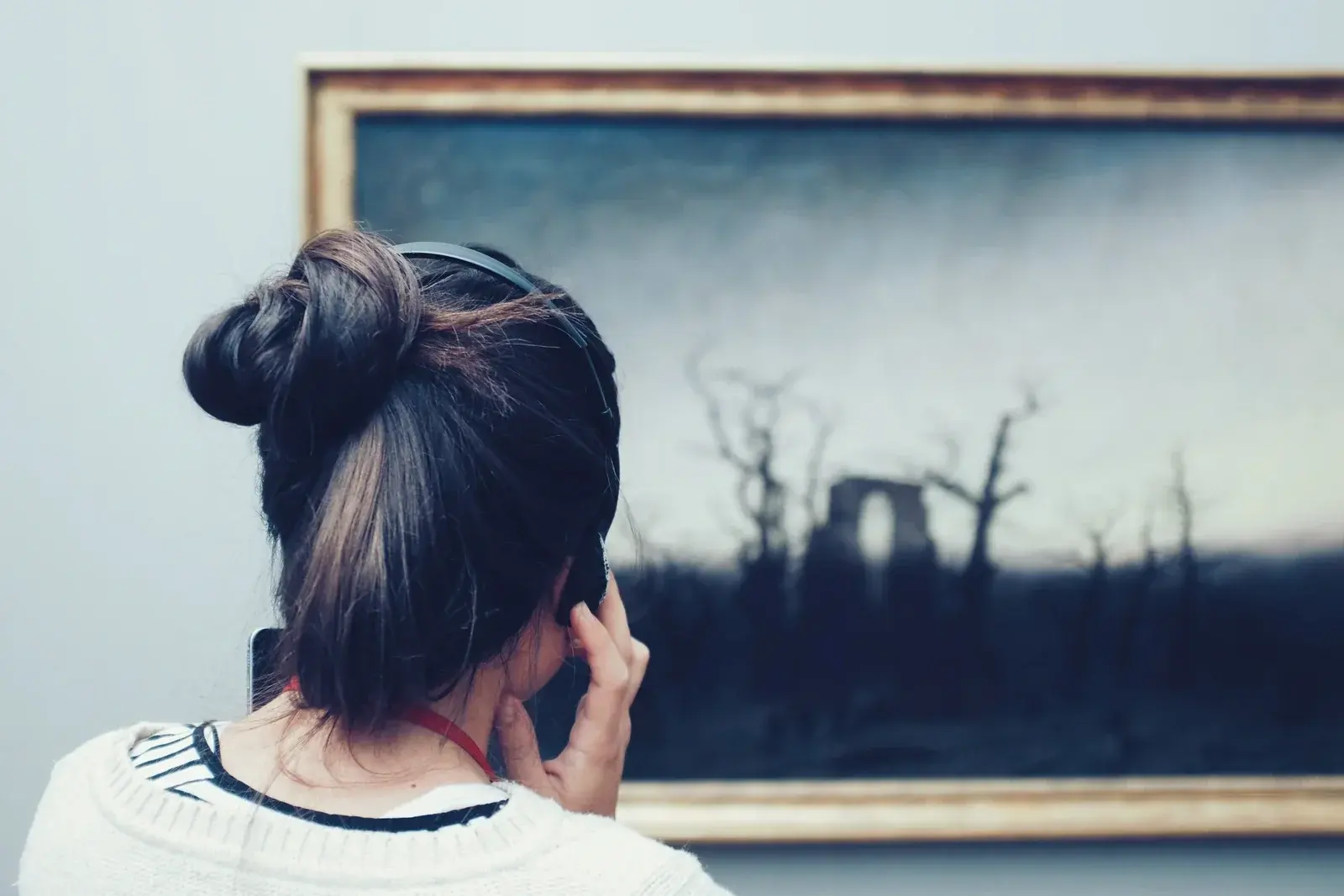 A visitor with an audio guide studies a dark romantic landscape painting of a ruined abbey in a gilt frame