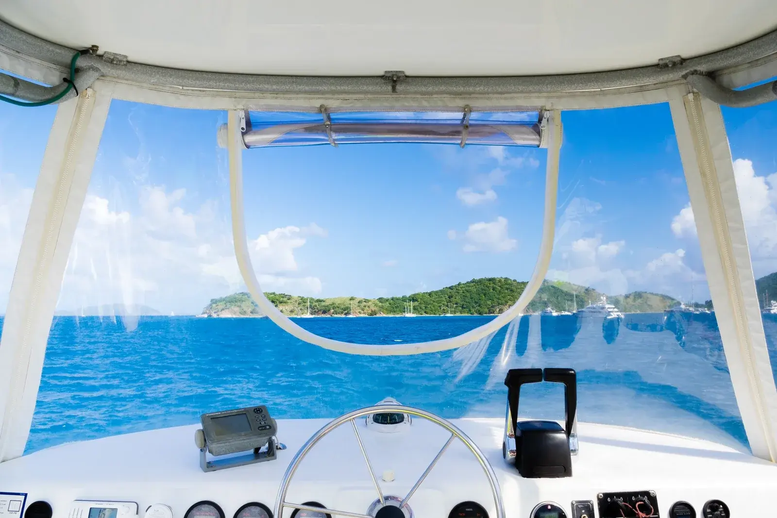The view from a motor yacht's helm across turquoise water to a green island, superyachts at anchor in the bay