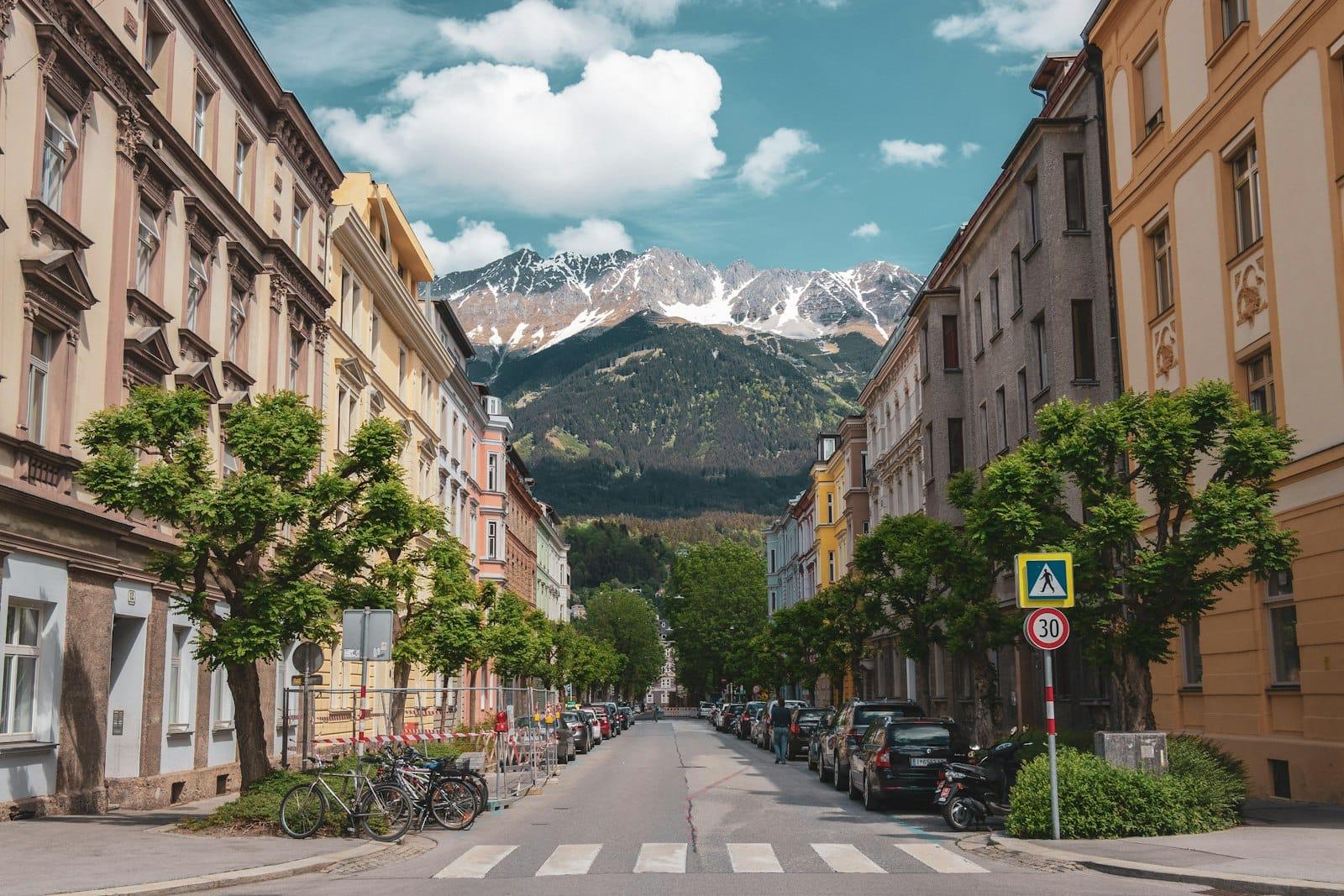 An alpine town street lined with pastel houses, a snow-capped ridge closing the view