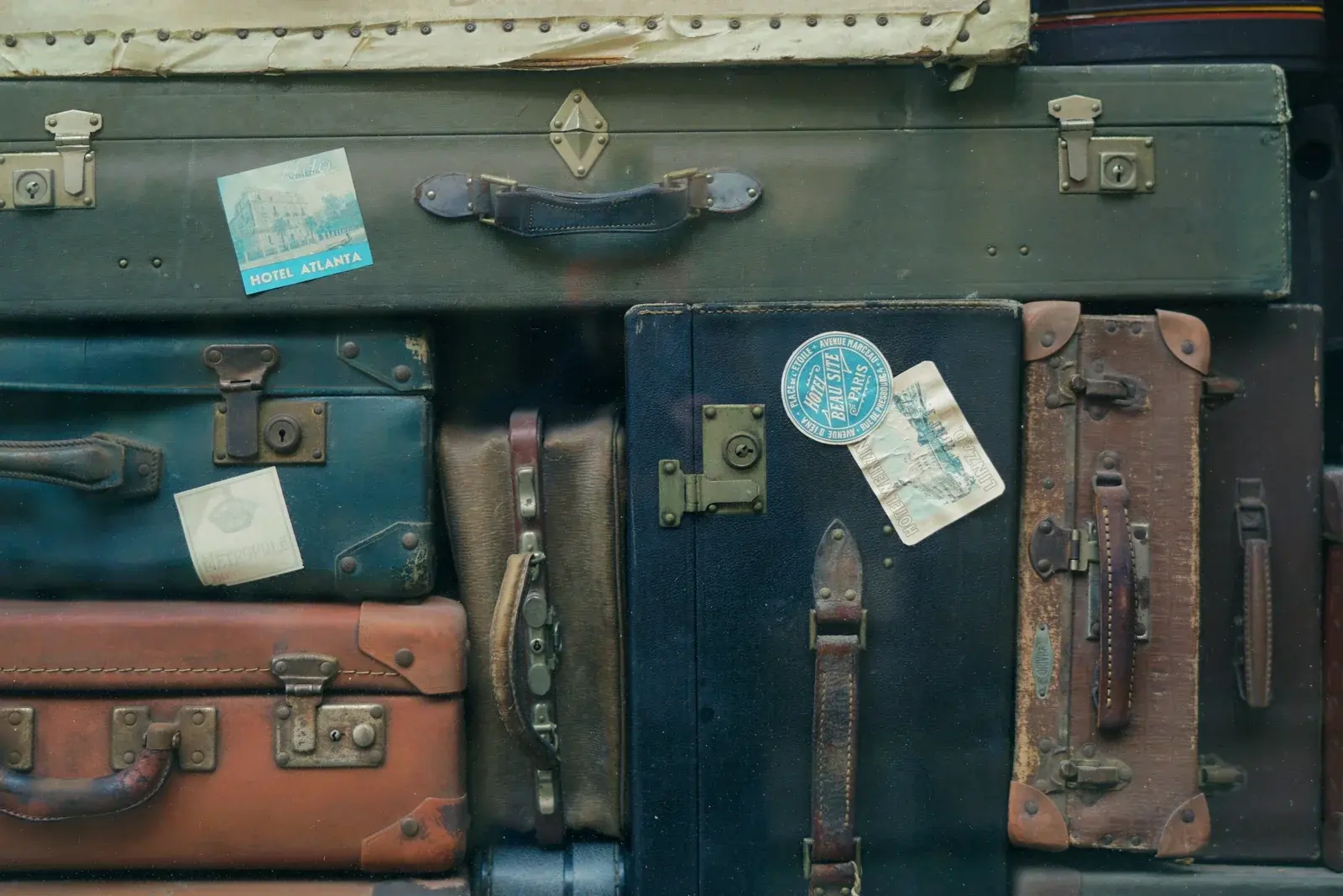 A stack of vintage leather and canvas suitcases with brass clasps and old hotel labels