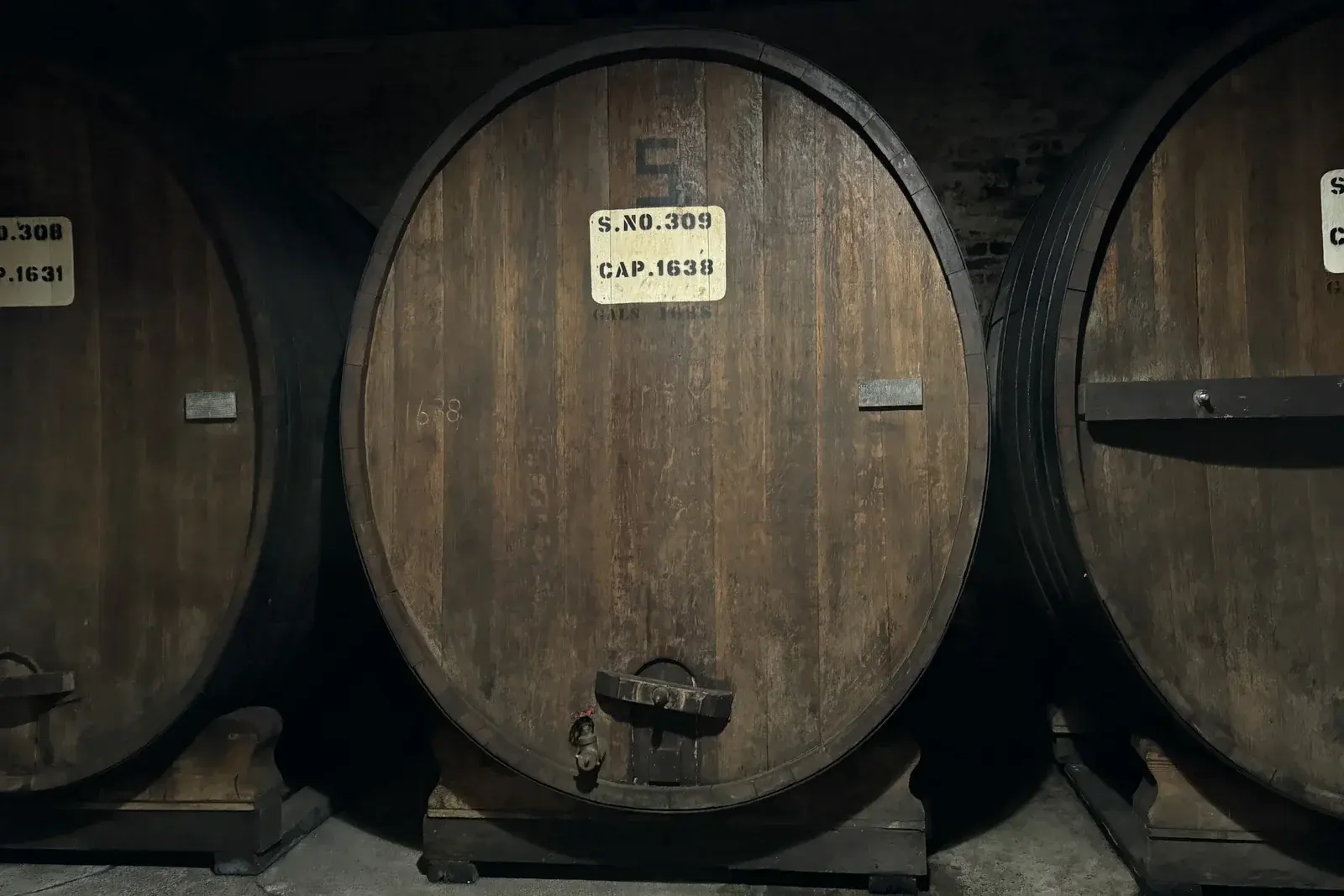 Giant oak wine casks with stencilled serial numbers resting in a dim brick cellar