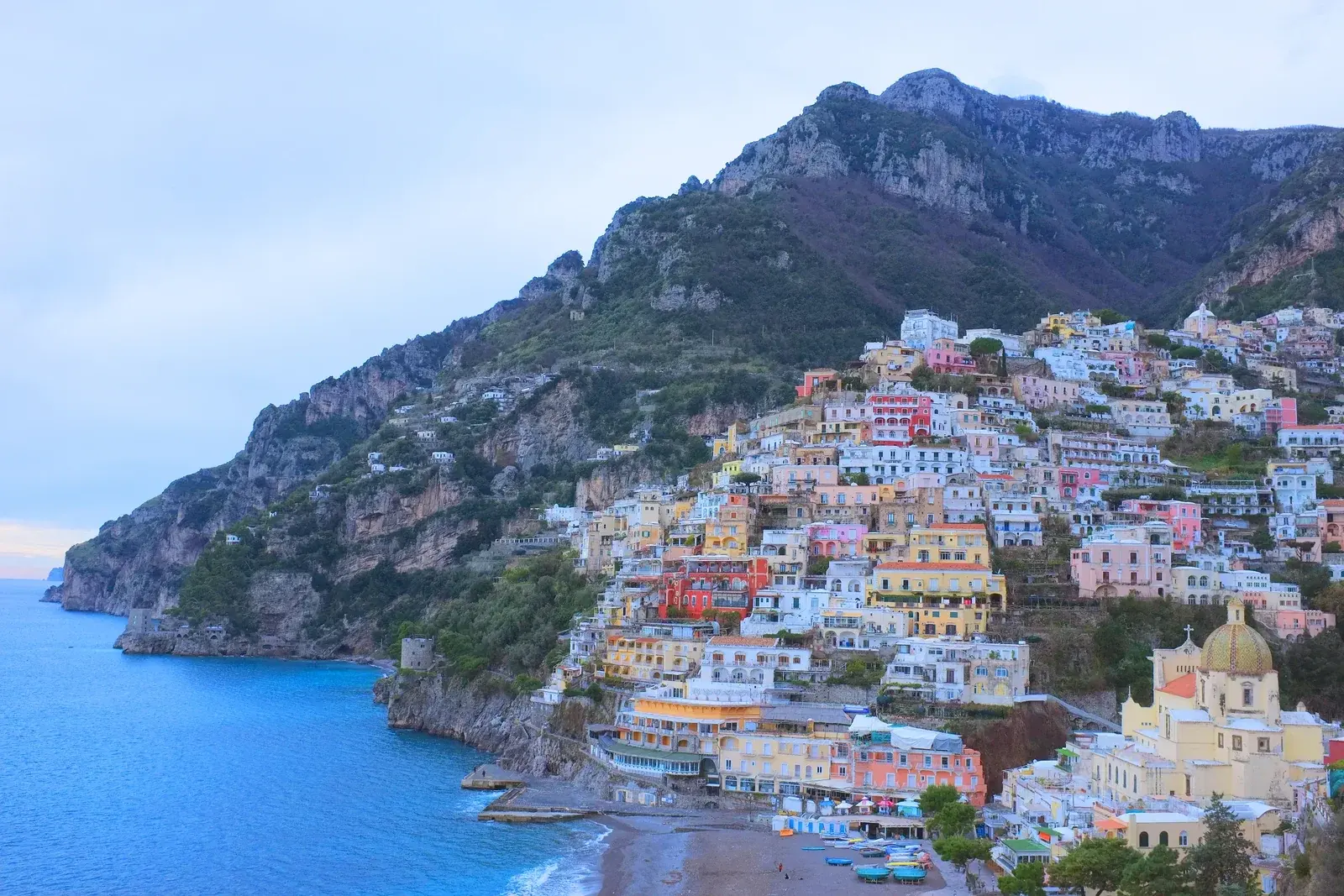 Positano's pastel houses stacked up the cliffs of the Amalfi Coast above a small beach and deep blue sea