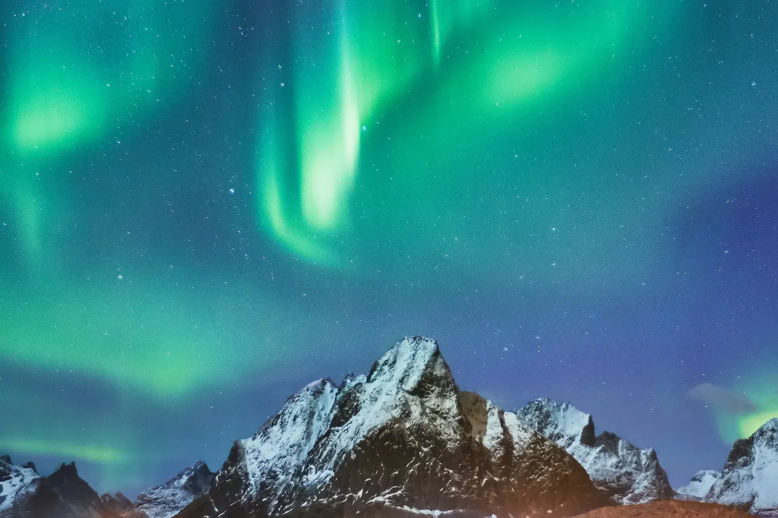 Green aurora borealis curling above snow-covered peaks near Reine in the Lofoten Islands, Norway