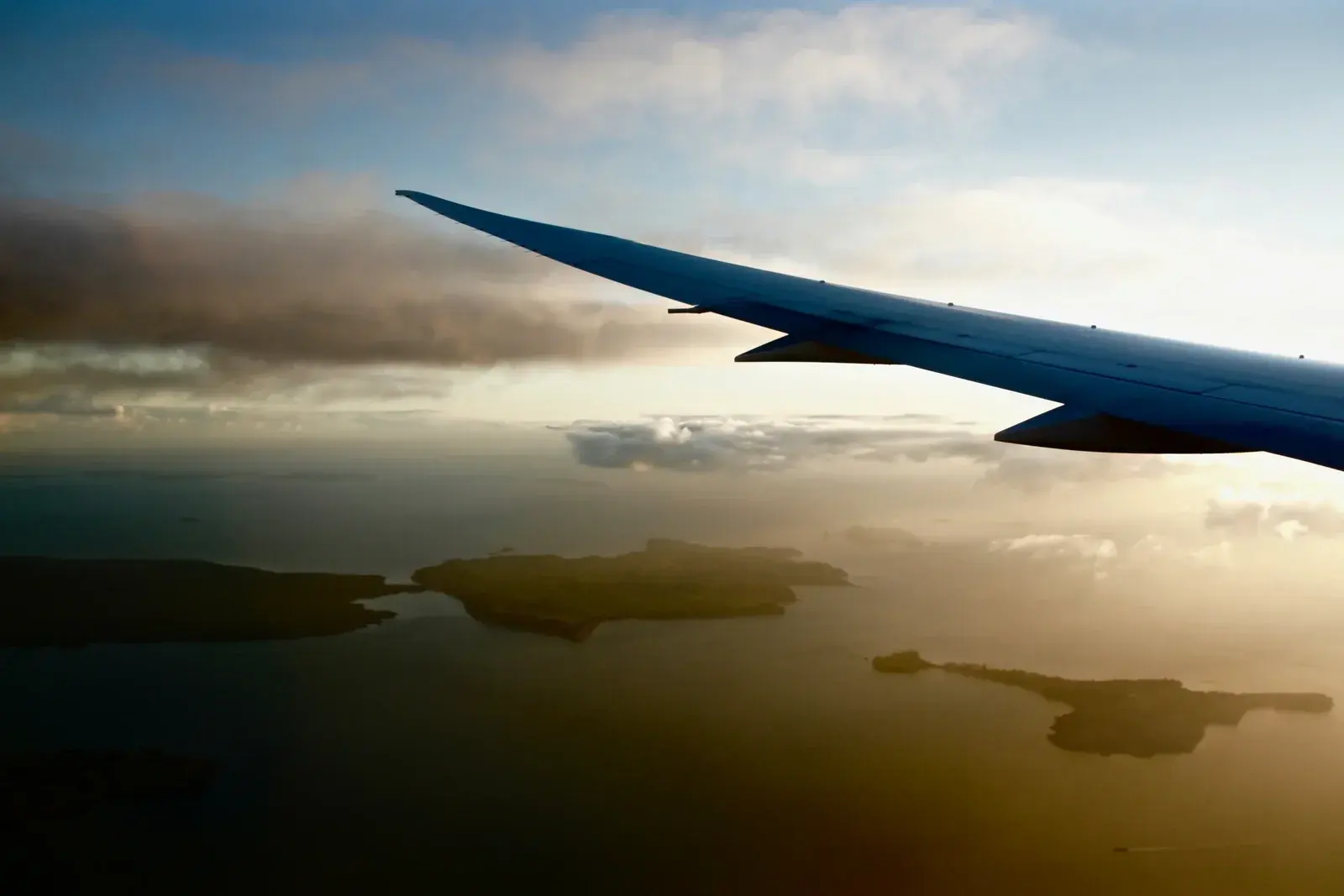 An aircraft wing over a chain of wooded islands at golden hour, low cloud on the horizon