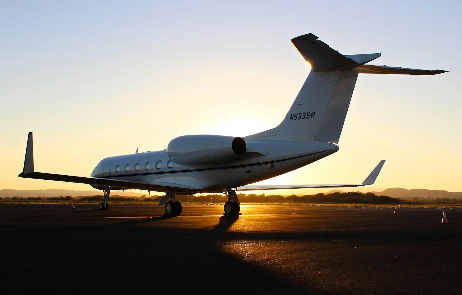 A private jet parked on an apron at sunset, its tail number lit by the low sun
