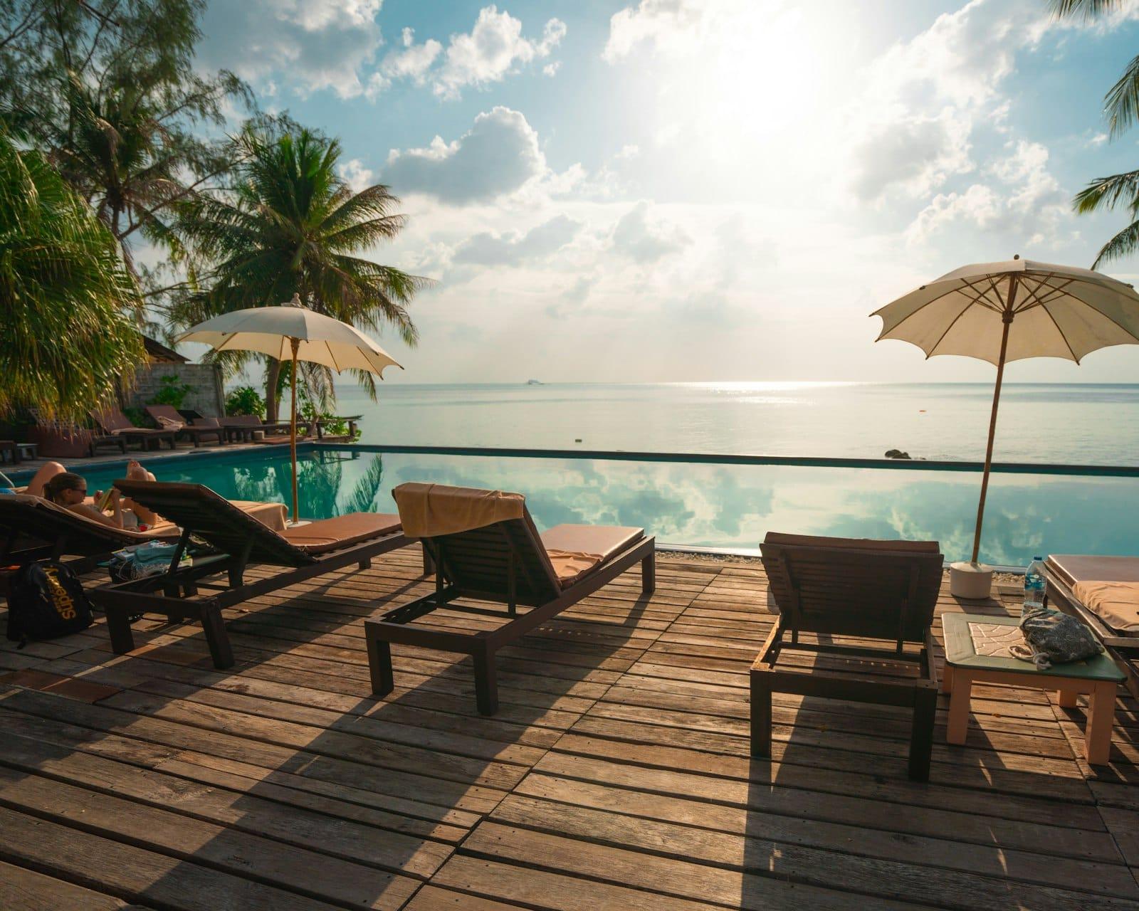 Wooden sun loungers and parasols on a deck beside a pool that meets the sea