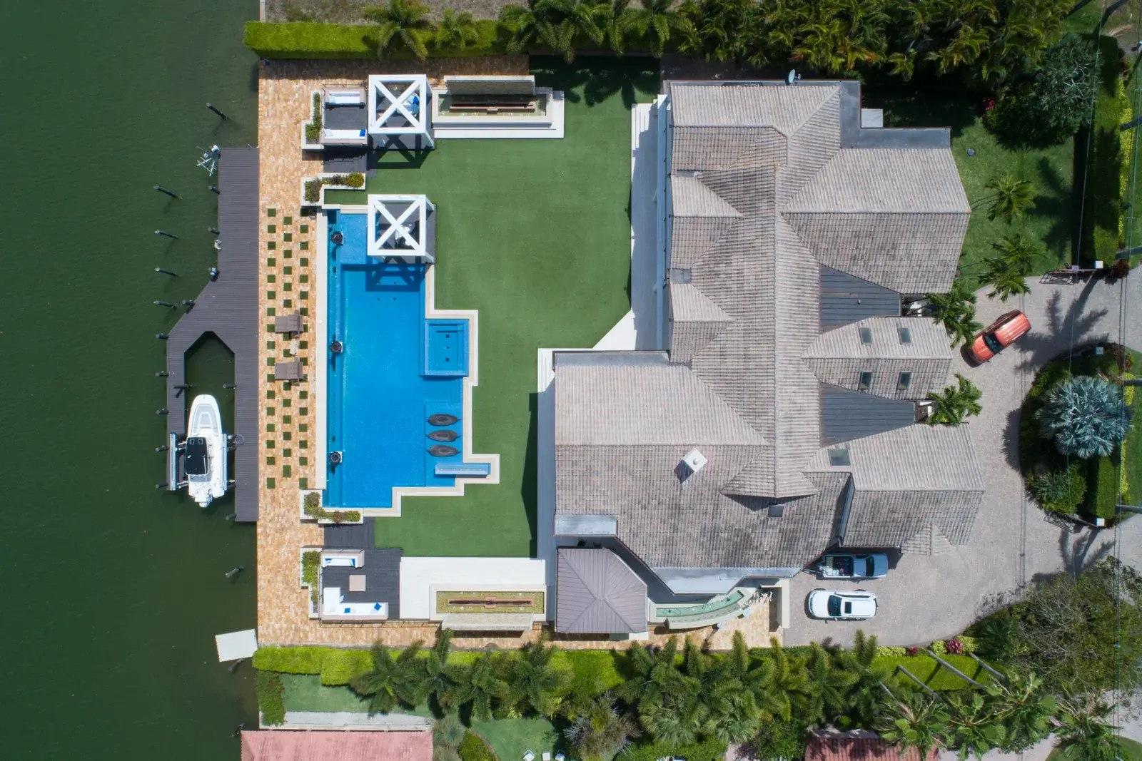 Aerial view of a waterfront estate with a long blue pool, lawn, private dock and moored boat