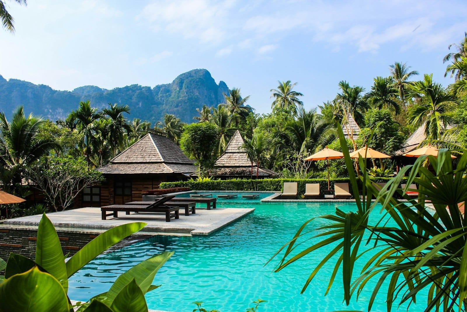 A resort pool ringed by pitched-roof pavilions and palms, limestone peaks behind