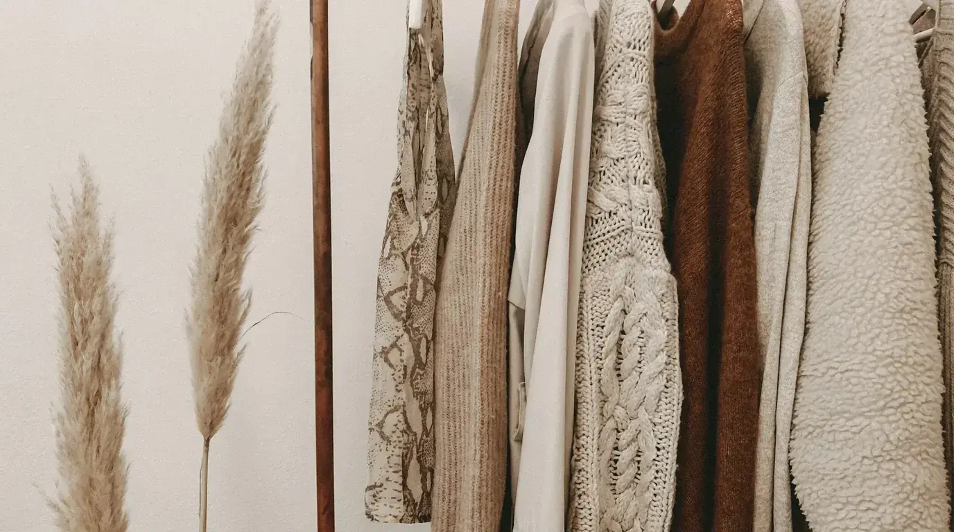 Wool, knit and shearling coats hanging in a row beside dried pampas grass