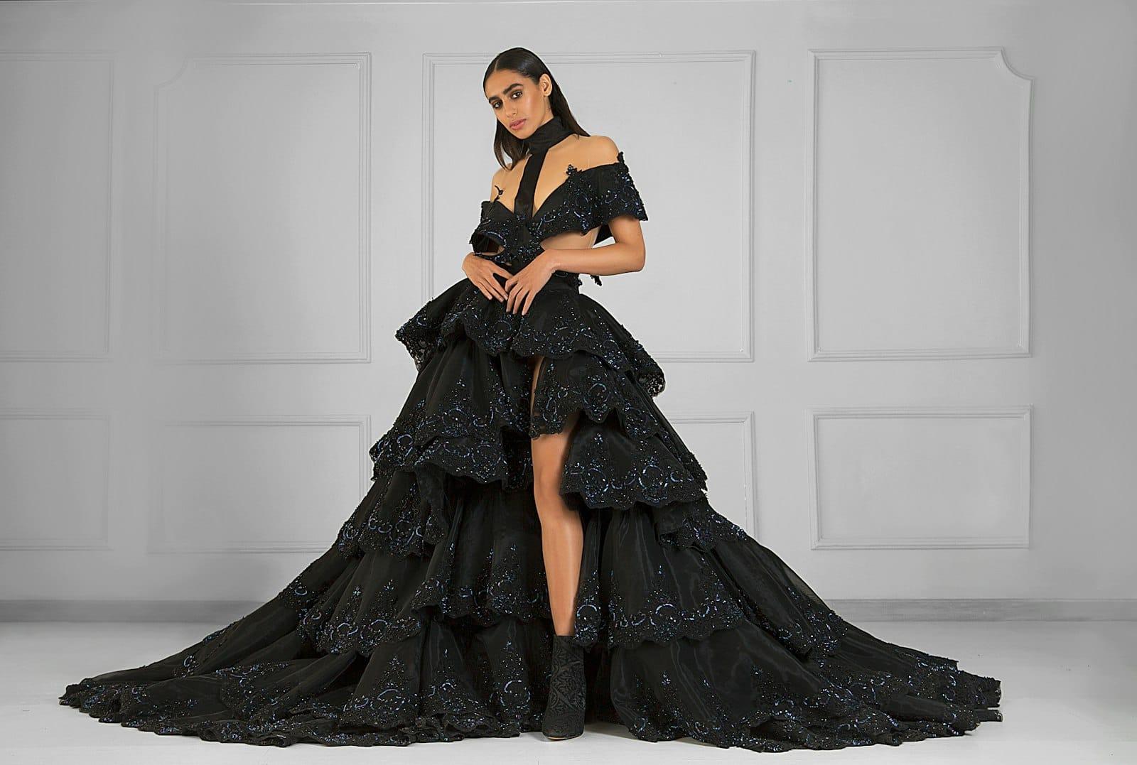 A model in a tiered black organza gown with a long train against a white panelled wall