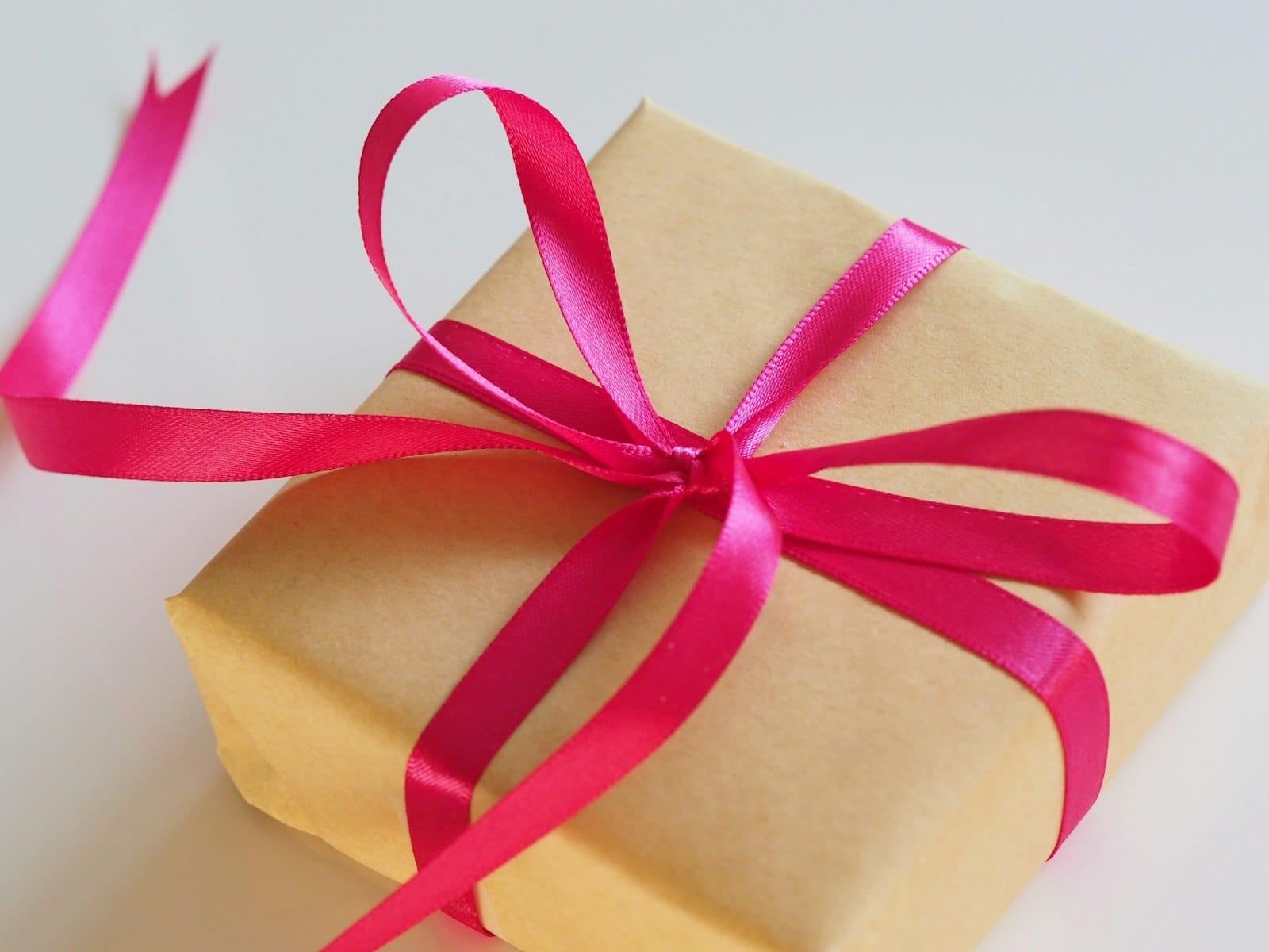A parcel in brown kraft paper tied with a bright pink satin ribbon on a white surface