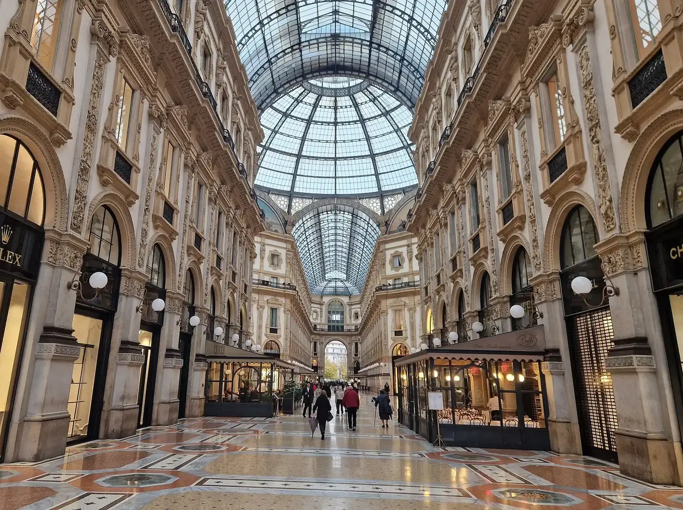 The glass-roofed arcade of the Galleria Vittorio Emanuele II in Milan, lined with shopfronts and cafes under an iron and glass dome