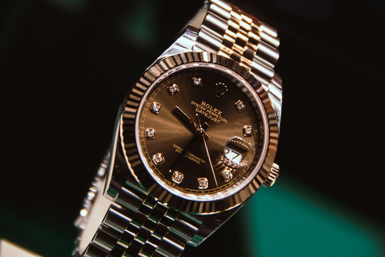 A close-up of a steel wristwatch with a fluted bezel, brown dial and diamond hour markers