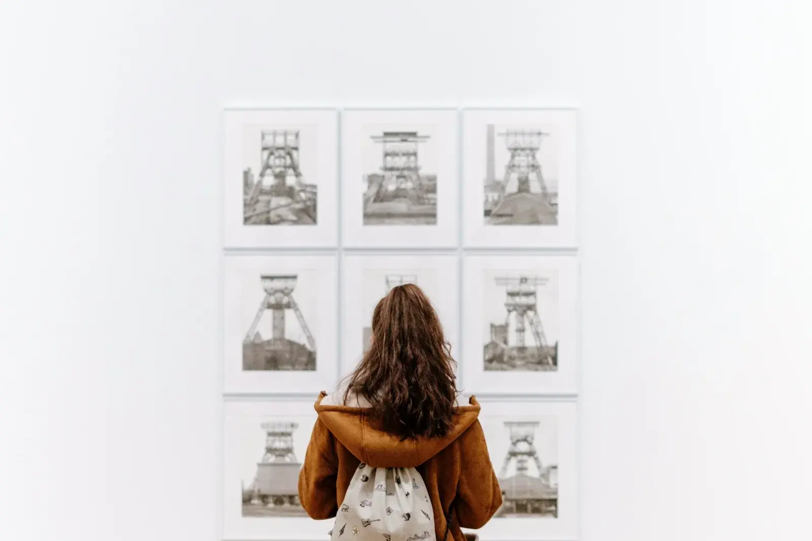 A visitor stands before a grid of nine framed black-and-white photographs on a white gallery wall