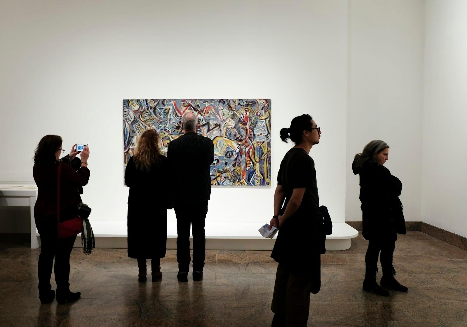 Gallery visitors in front of a large abstract painting, one of them photographing it on a phone