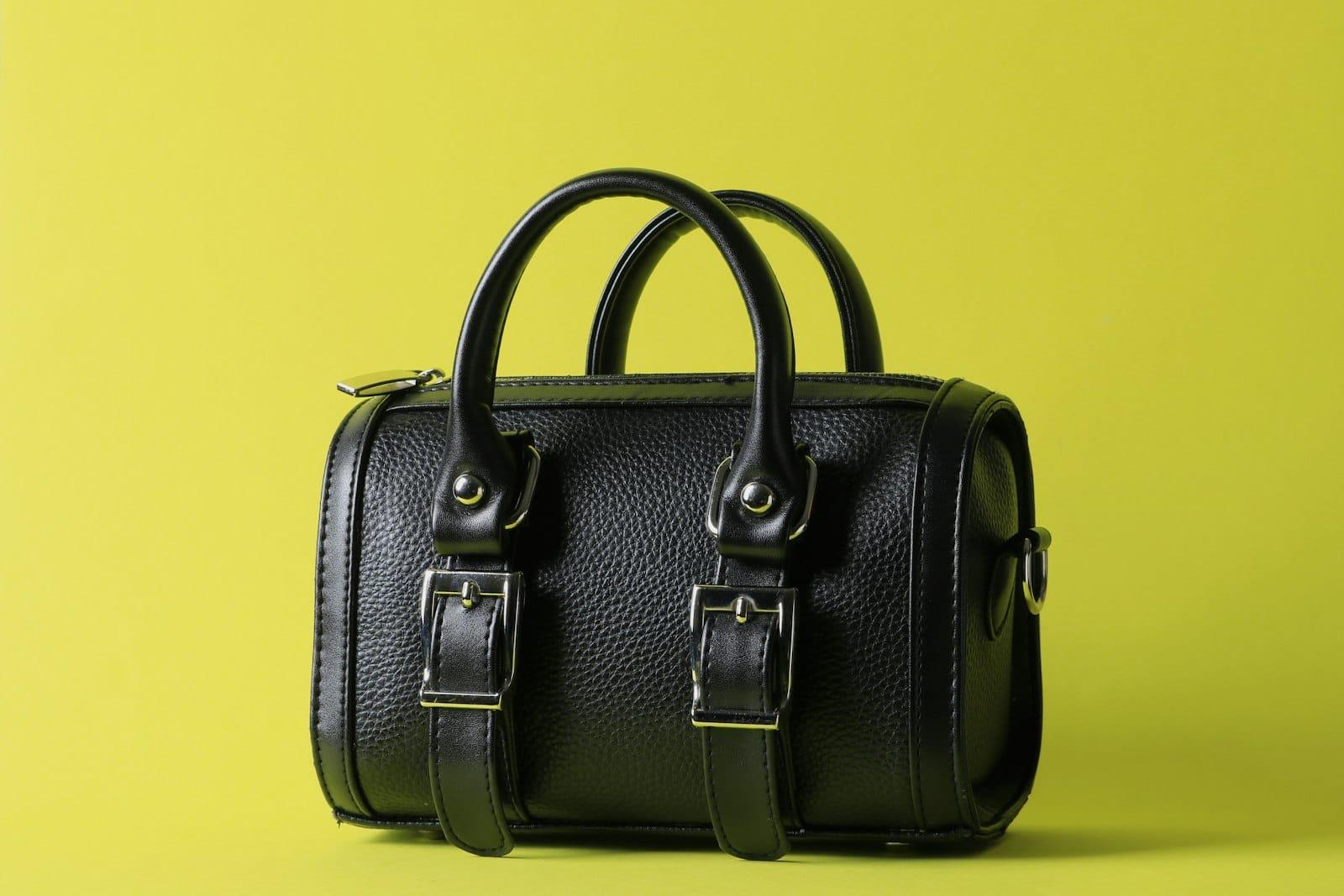 A black leather handbag with twin buckled straps and rolled handles against a lime background