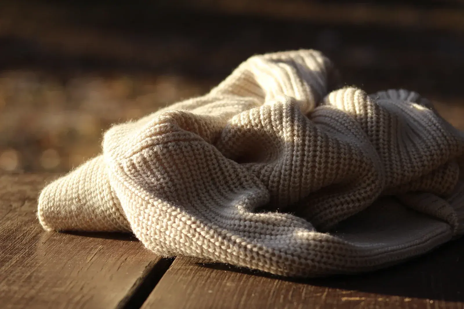 A cream ribbed-knit jumper lying on weathered wooden boards in low golden sunlight