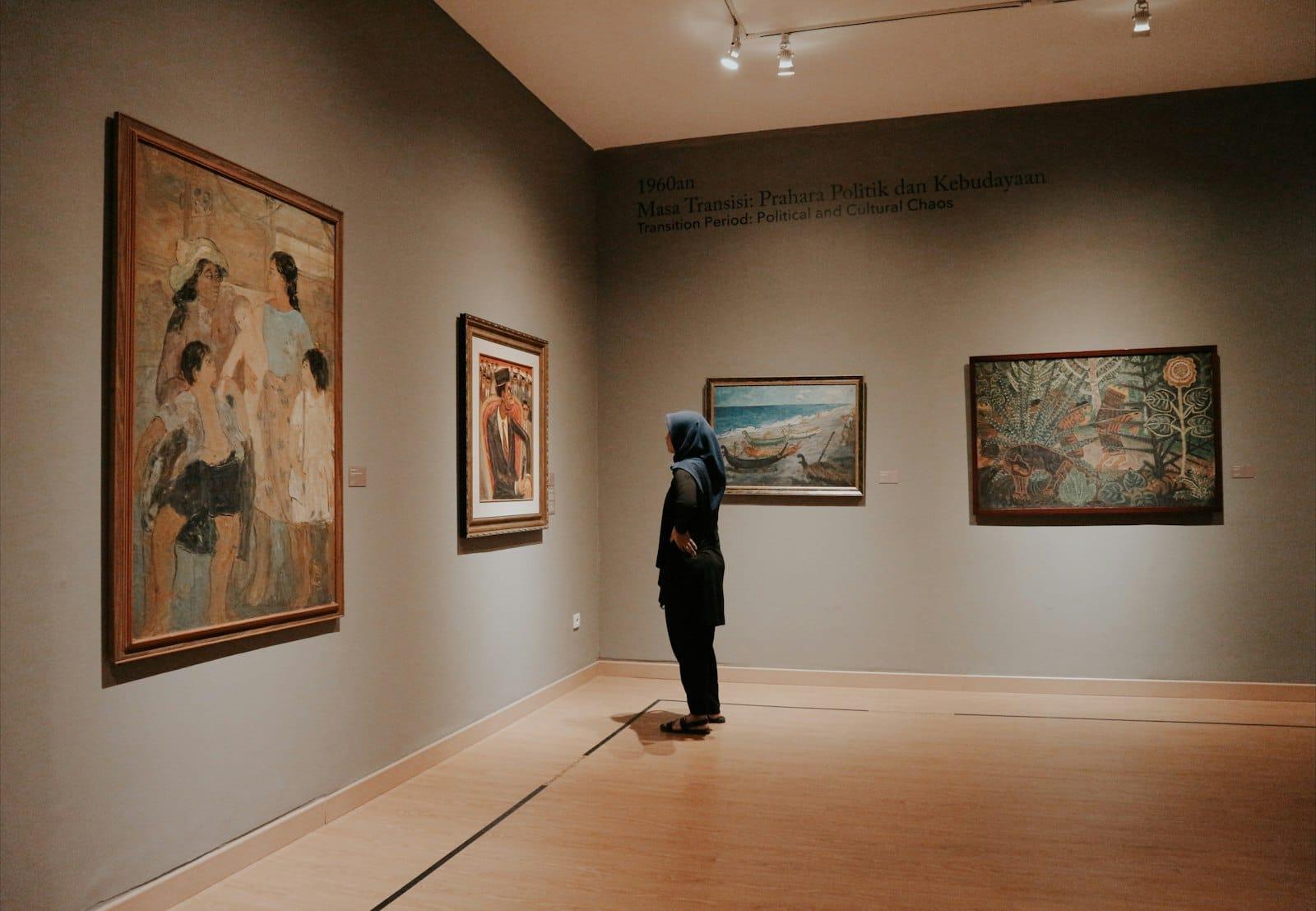 A visitor in a gallery of framed mid-century paintings beneath a wall text panel