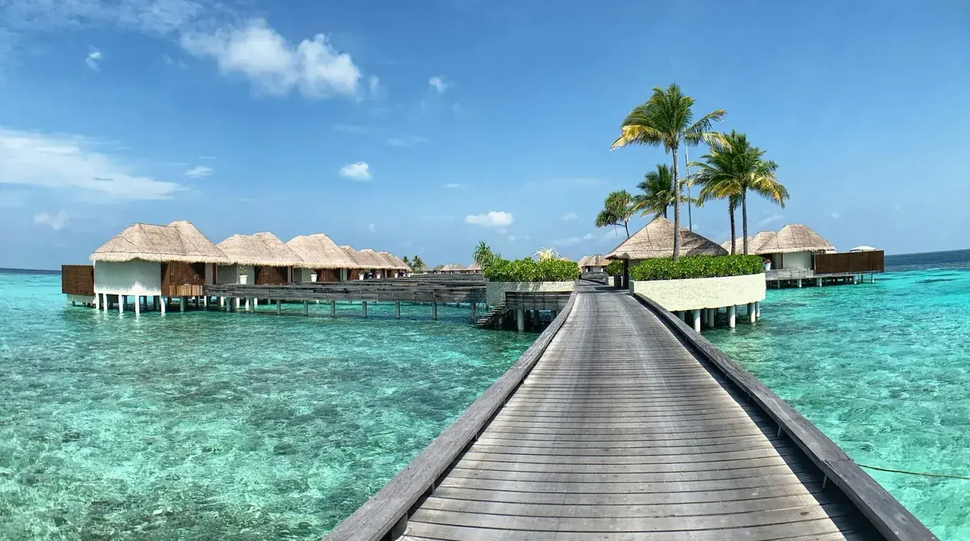 A timber boardwalk running out to thatched overwater villas above turquoise shallows